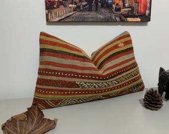 May include: A decorative pillow with a striped pattern in shades of red, brown, beige, and yellow. The pillow is made of woven fabric and has a traditional design.