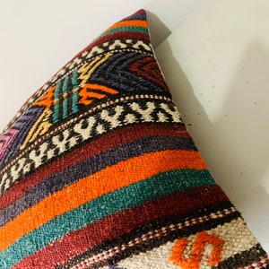 May include: A colorful woven pillow cover with a geometric pattern in shades of orange, teal, purple, and brown. The pillow cover is made of a soft, textured fabric.