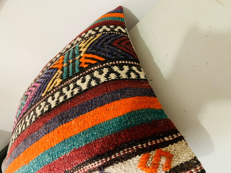 May include: A colorful woven pillow cover with a geometric pattern in shades of orange, teal, purple, and brown. The pillow cover is made of a soft, textured fabric.