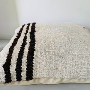 May include: A white throw pillow with three black stripes down one side. The pillow is made of a soft, textured fabric.