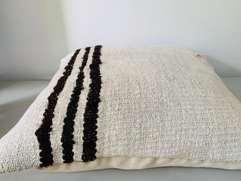 May include: A white throw pillow with three black stripes down one side. The pillow is made of a soft, textured fabric.