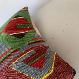 May include: A colorful throw pillow with a geometric pattern in shades of red, green, blue, and yellow. The pillow is made of woven fabric and has a textured surface.