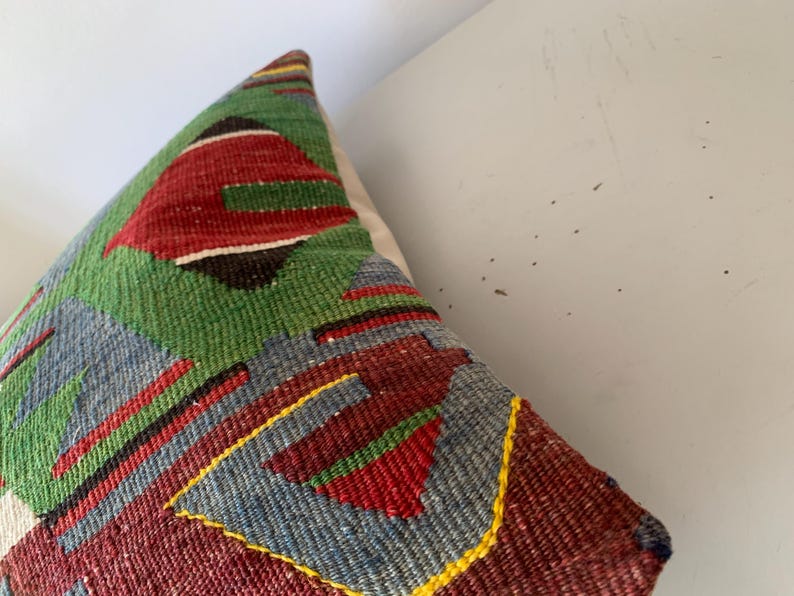 May include: A colorful throw pillow with a geometric pattern in shades of red, green, blue, and yellow. The pillow is made of woven fabric and has a textured surface.