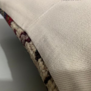 Puede incluir: Primer plano de una funda de almohada blanca con un borde de tela estampada de colores. La tela es una mezcla de beige, marr&oacute;n, rojo y azul.