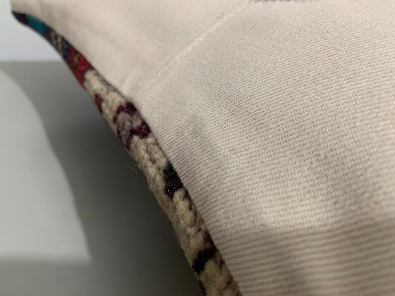 Puede incluir: Primer plano de una funda de almohada blanca con un borde de tela estampada de colores. La tela es una mezcla de beige, marr&oacute;n, rojo y azul.