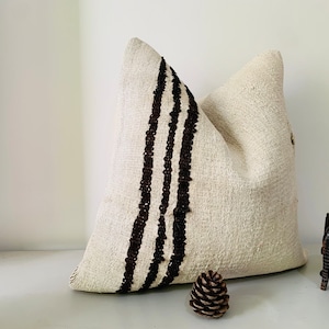 May include: A white throw pillow with three black stripes down the side. The pillow is made of a soft, textured fabric.