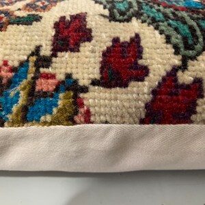 Puede incluir: Primer plano de una almohada de color crema con un estampado floral colorido. La almohada tiene un borde blanco y est&aacute; hecha de una tela suave y texturizada.