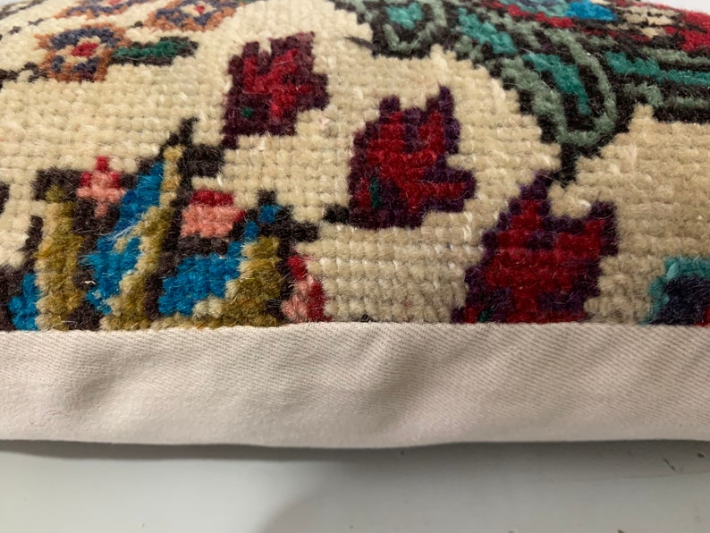 Puede incluir: Primer plano de una almohada de color crema con un estampado floral colorido. La almohada tiene un borde blanco y est&aacute; hecha de una tela suave y texturizada.