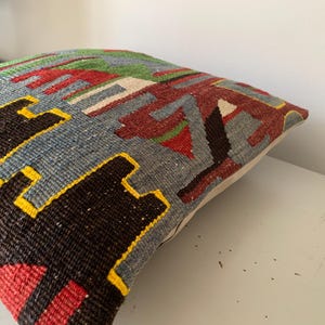 May include: A colorful throw pillow with a geometric pattern in shades of red, blue, green, yellow, and black. The pillow is made of woven fabric and has a white backing.