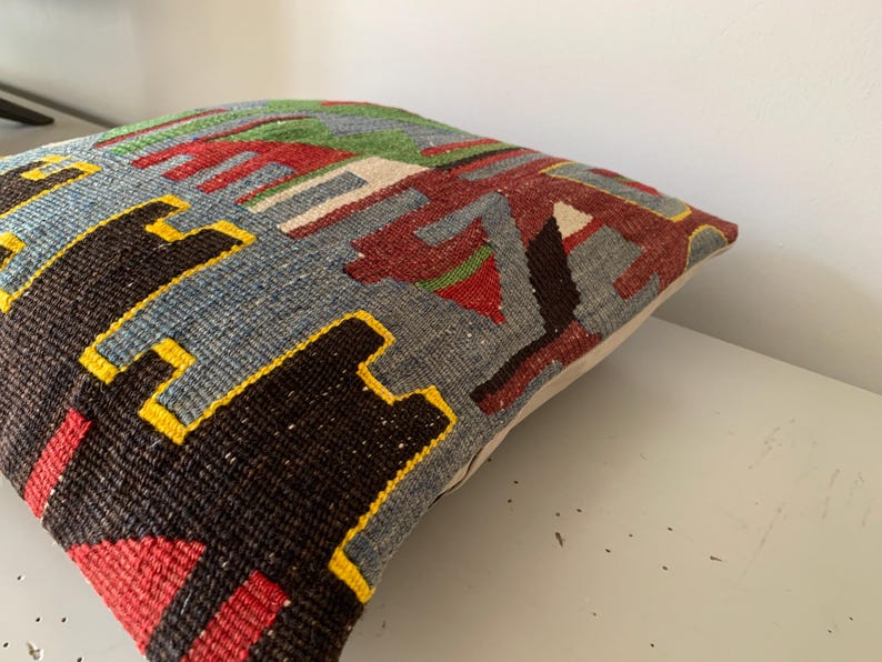 May include: A colorful throw pillow with a geometric pattern in shades of red, blue, green, yellow, and black. The pillow is made of woven fabric and has a white backing.