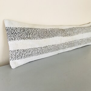 May include: A long white and black striped bolster pillow with a subtle speckled pattern.