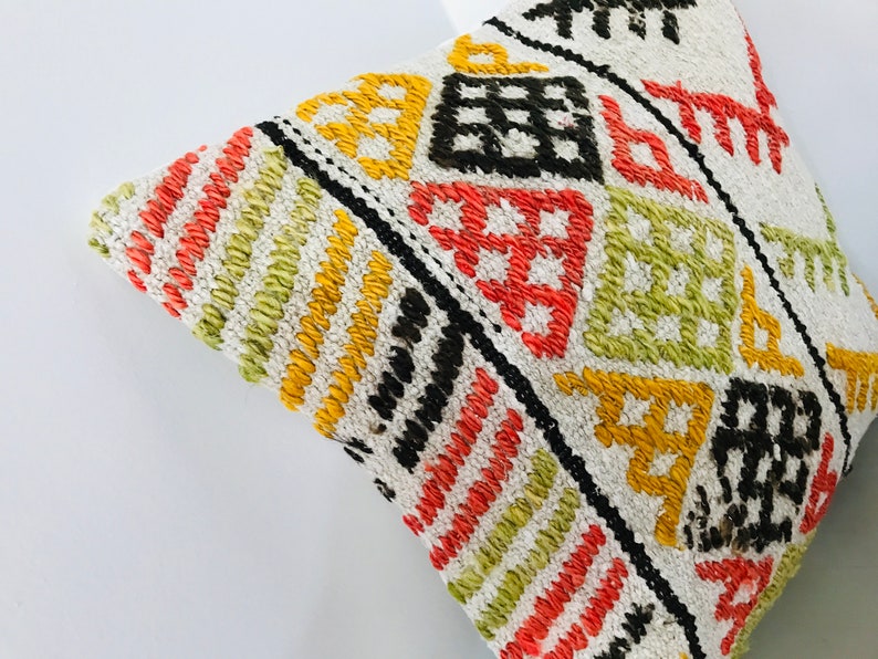 Puede incluir: Una almohada blanca con un patr&oacute;n geom&eacute;trico colorido en tonos de rojo, naranja, amarillo, verde y negro. El patr&oacute;n est&aacute; tejido en la tela y crea un aspecto texturizado.