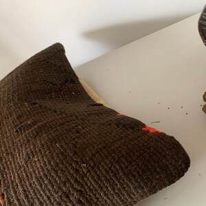 May include: A brown and orange woven throw pillow with a textured surface.