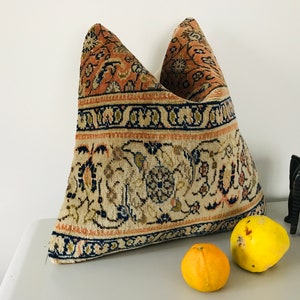 May include: A decorative pillow with a beige, pink, and blue floral pattern. The pillow is made from a woven fabric and has a fringed edge.