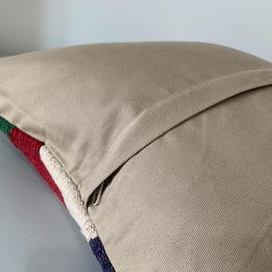 May include: A beige pillow with a zipper closure. The pillow has a colorful striped pattern on the front.
