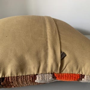 May include: A tan pillow with a zipper closure and a brown, orange, and white geometric pattern on the front.