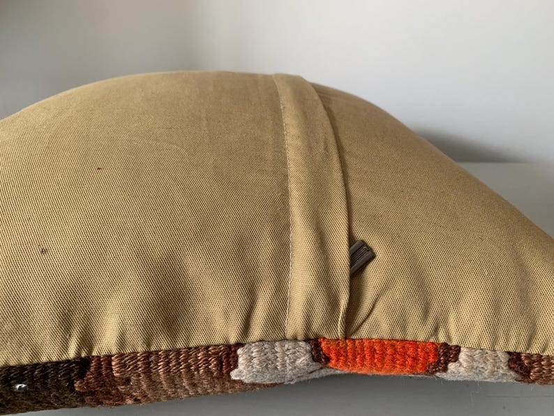 May include: A tan pillow with a zipper closure and a brown, orange, and white geometric pattern on the front.