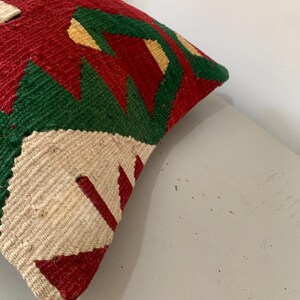 May include: A colorful throw pillow with a geometric pattern in shades of red, green, white, and yellow. The pillow is made of a woven fabric and has a slightly textured surface.