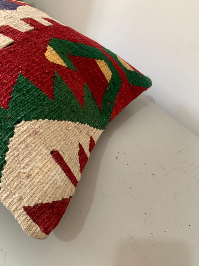 May include: A colorful throw pillow with a geometric pattern in shades of red, green, white, and yellow. The pillow is made of a woven fabric and has a slightly textured surface.