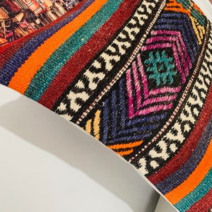 May include: A colorful throw pillow with a geometric pattern in shades of orange, red, blue, green, and white. The pillow is made of woven fabric and has a fringed edge.