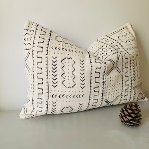 Könnte beinhalten: Ein weißes Kissen mit einem schwarzen geometrischen Muster. Das Kissen ist aus einem weichen, strukturierten Stoff.