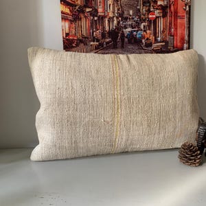 May include: Cream-colored rectangular pillow with a textured surface. The pillow has a vertical yellow stripe down the center. A wooden elephant figurine and a pine cone are next to the pillow.