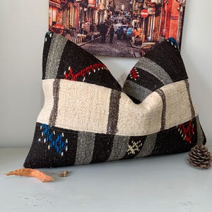 May include: A black, white, and gray patterned pillow with red and blue accents. The pillow is made of woven fabric and has a rectangular shape.