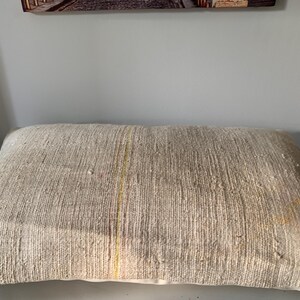 May include: A rectangular beige pillow with a textured, woven appearance. The pillow has a subtle vertical stripe of yellow and red. The pillow is a neutral color and would complement many decor styles.