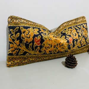 May include: A decorative cushion with a floral pattern in shades of gold, orange, and black on a dark blue background. The cushion is made of a soft, plush fabric.