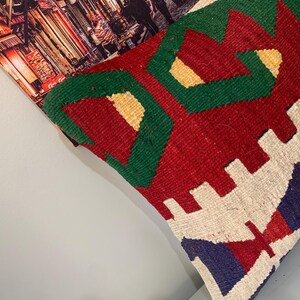May include: A colorful throw pillow with a geometric pattern in shades of red, green, white, and blue. The pillow is made of woven fabric and has a textured surface.
