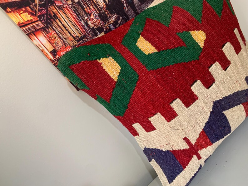 May include: A colorful throw pillow with a geometric pattern in shades of red, green, white, and blue. The pillow is made of woven fabric and has a textured surface.