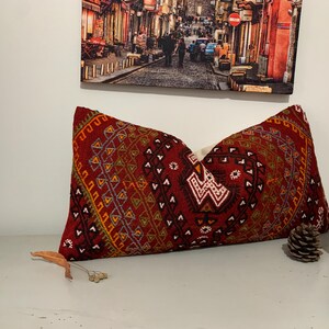May include: A red, orange, and blue patterned throw pillow with a geometric design. The pillow is made of a soft, woven fabric.