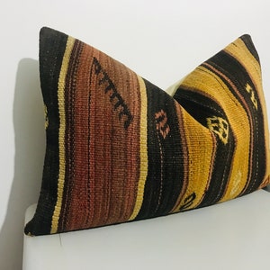 May include: A decorative pillow with a woven design. The pillow features vertical stripes in shades of brown, black, and gold. The pillow is rectangular and appears to be made of a textured fabric, adding a rustic touch to home decor.