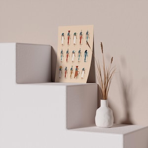 Puede incluir: Una impresi&oacute;n beige con ilustraciones de dioses y diosas egipcios. La impresi&oacute;n presenta una variedad de figuras con diferentes tocados y vestimentas. La impresi&oacute;n est&aacute; enmarcada y se exhibe en un estante blanco.