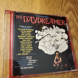 May include: A CD case with a black background and the title "The Daydreamer" in white text. The case features a colorful illustration of a child dreaming, surrounded by fantastical creatures. The back of the case lists the cast and crew of the film.