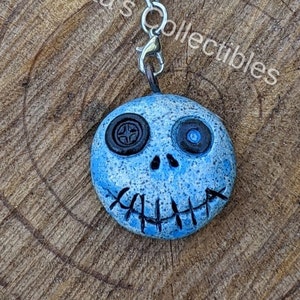 May include: A blue and white ceramic charm with a stitched-on mouth and button eyes. The charm is attached to a silver metal chain.