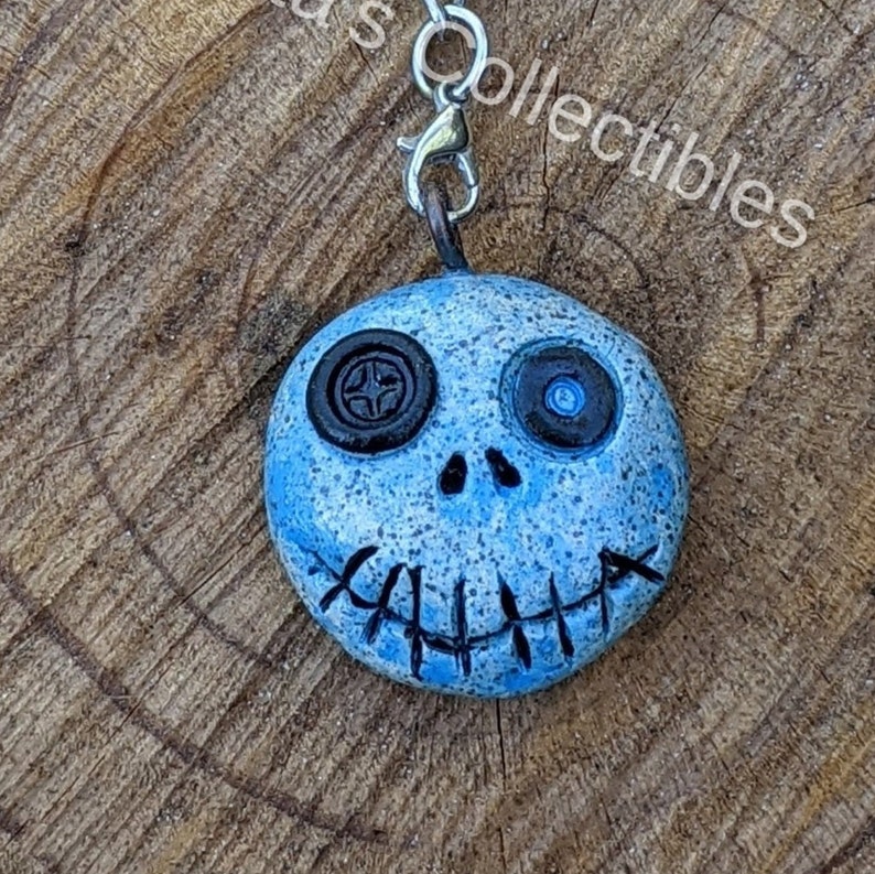 May include: A blue and white ceramic charm with a stitched-on mouth and button eyes. The charm is attached to a silver metal chain.