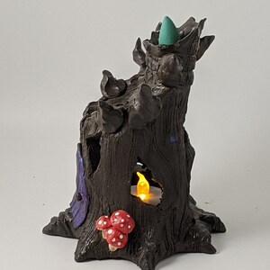 May include: A ceramic incense burner shaped like a tree stump with a teal incense cone in the top, a small candle in a hole, and red and white mushrooms at the base.