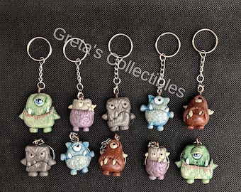 May include: Ten colourful monster keychains with different expressions and details. Each keychain features a unique monster design with a silver key ring.