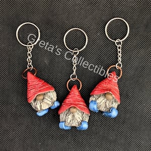 May include: Three red and white gnome keychains with blue boots. Each gnome has a white beard and a red hat. The keychains are attached to silver key rings.