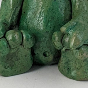 May include: A green ceramic figurine of a creature with a textured surface and three toes on each foot.