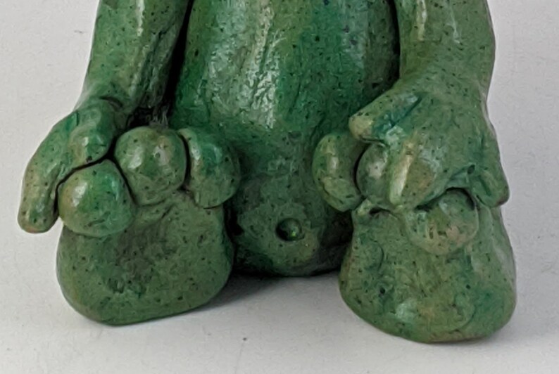 May include: A green ceramic figurine of a creature with a textured surface and three toes on each foot.