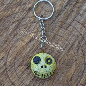 May include: Yellow and black clay charm with a stitched mouth and button eyes on a silver key chain.
