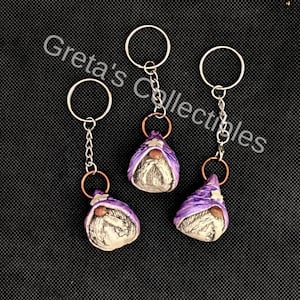 May include: Three purple gnome keychains with white beards and white hats. Each gnome has a silver chain and a silver ring.