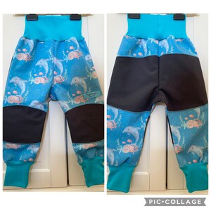 Könnte beinhalten: Hose mit blauem Unterwassermotiv aus Delfinen, Korallen und Muscheln. Das Kleidungsstück hat einen breiten türkisfarbenen Bund und Beinabschlüsse sowie schwarze Einsätze an Knien und Gesäß. Ein kleines Etikett trägt die Aufschrift Tingelange.