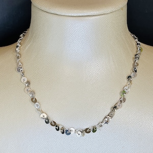 Może przedstawiać: Srebrny naszyjnik z łańcuszkiem wykonanym z małych, okrągłych, płaskich dysków.