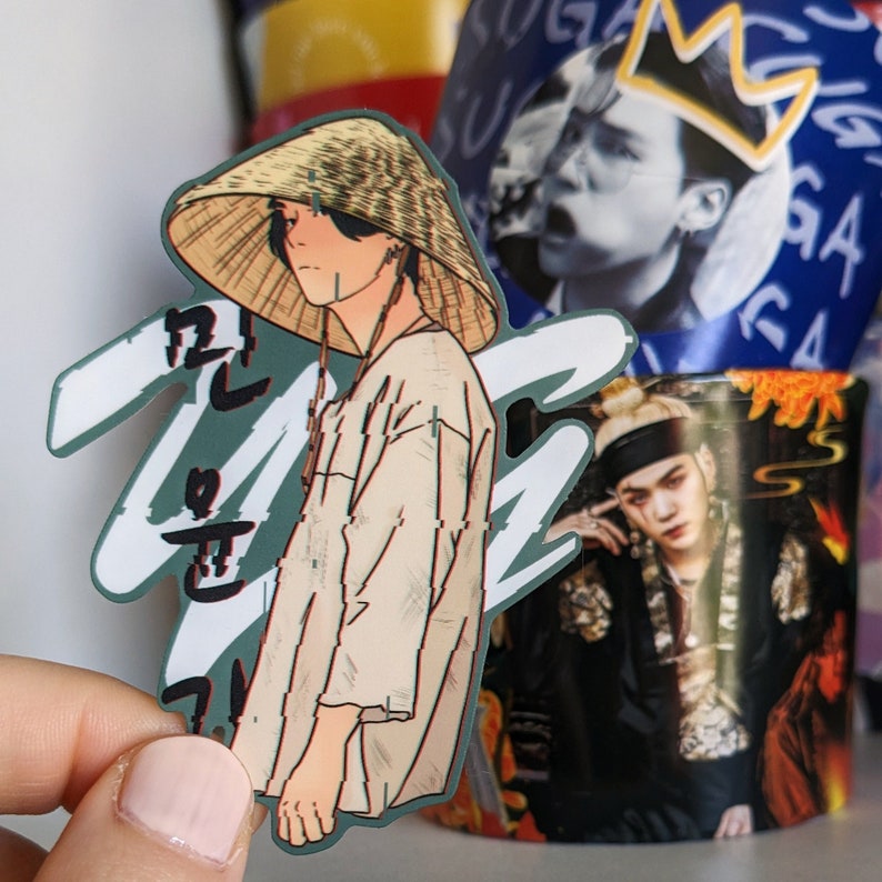 May include: A sticker featuring a cartoon illustration of a person wearing a straw hat and a beige shirt. The person is standing in front of a green and white background with Korean text.