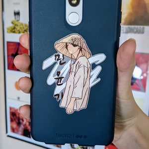 May include: A teal blue phone case with a white sticker of a person wearing a straw hat and a long-sleeved shirt. The sticker has Korean text that reads "Run, Run, Run". The phone case has the text "tech21" printed on the bottom.