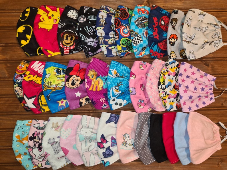May include: A collection of 28 colorful fabric face masks with various cartoon characters and designs. The masks are arranged in three rows, with the top row featuring characters like Batman, Pikachu, and Harry Potter. The middle row features characters like SpongeBob SquarePants, Mickey Mouse, and Frozen's Elsa. The bottom row features characters like a unicorn, a cat, and a bunny.