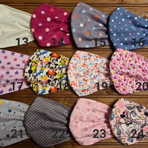 May include: Twenty-four different fabric face masks with various patterns, including polka dots, stars, flowers, and cartoon characters. The masks are numbered 13 through 24.